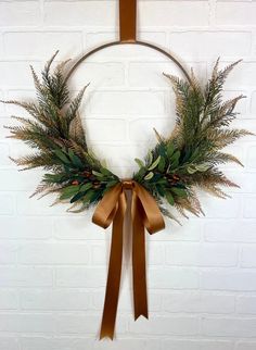 a wreath hanging on a brick wall with a brown ribbon around it and some greenery