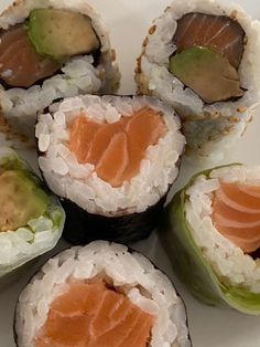 sushi rolls with avocado and salmon are arranged in a circle on a white plate