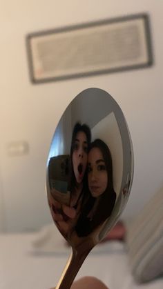 a person holding a spoon with a reflection of two people in the mirror on it