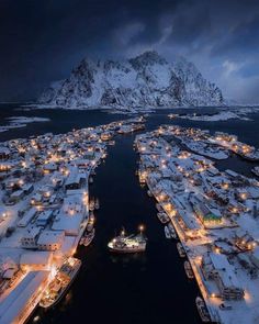 an aerial view of boats in the water at night with snow covered mountains in the background