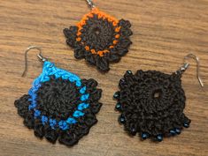 two crocheted earrings with blue and orange beads sitting on top of a wooden table