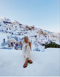 a woman sitting on top of a roof next to a white building with lots of buildings in the background