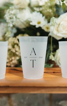 three shot glasses sitting on top of a wooden table next to white flowers and greenery