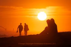 two people are sitting on the beach watching the sun go down