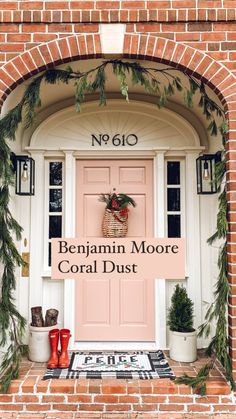 a pink front door decorated with christmas greenery and red boots for the holiday season