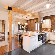 an open concept kitchen and dining room with exposed brick walls, white cabinets, hardwood flooring, and stainless steel appliances