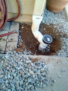 a drainage pipe that is in the ground next to some rocks and gravel with a hose connected to it