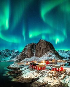 the northern lights shine brightly over houses and snow covered mountains in lofo, norway