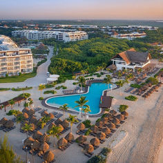 an aerial view of the resort and pool area at sunset, with thatched huts on either side