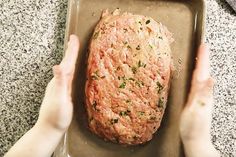 someone is holding their hands over a meatloaf on a baking sheet in the kitchen