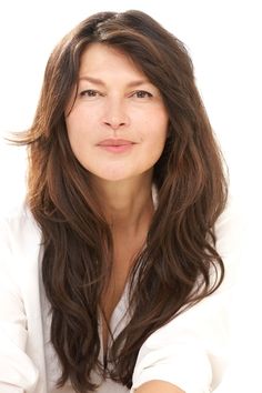 a woman with long brown hair and white shirt posing for the camera in front of a white background