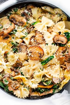 a skillet filled with pasta, mushrooms and spinach on top of a white table