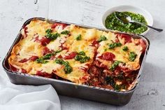 a casserole dish with meat, cheese and spinach garnished with pesto