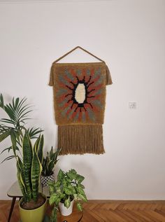 a wall hanging on the side of a white wall next to potted plants and a green plant