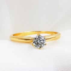 a yellow gold engagement ring with a single diamond on the top and bottom, sitting on a white cloth