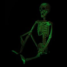 a skeleton sitting in the dark with its legs spread out and glowing green lights on it