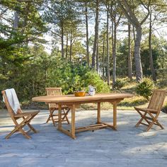 a wooden table and chairs sitting on top of a stone floor next to some trees