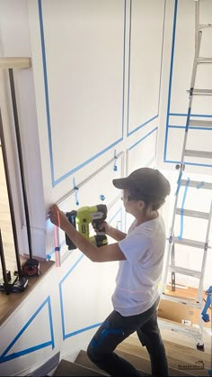 a young boy is painting the walls in his room with blue tape and a drill