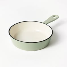 a green and white pan sitting on top of a white table next to a spoon