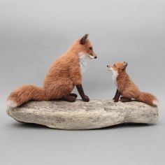 two stuffed foxes sitting on top of a rock