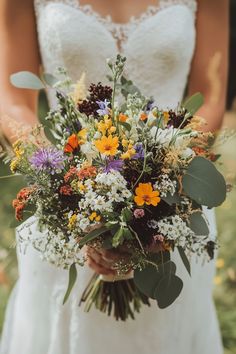 a bride holding a bouquet of wildflowers and greenery for her wedding day