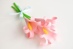 two pink flowers with green stems in a square container on a white surface, one flower has been cut into smaller pieces and the other is attached to a string