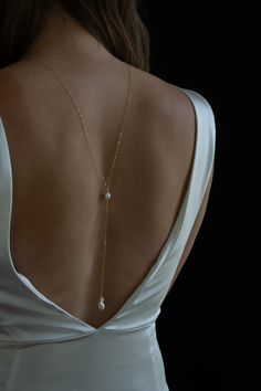 the back of a woman's white dress with a gold chain and pearls on it