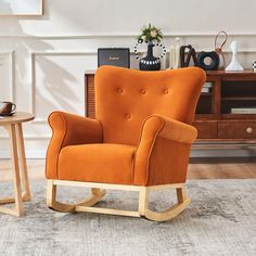 an orange rocking chair sitting on top of a rug next to a wooden table and cabinet