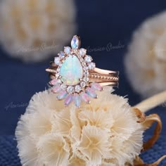 an opal and diamond ring sits on top of some fluffy white flowers, surrounded by feathers