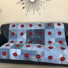 a couch covered in a blue and red plaid blanket next to a clock on the wall