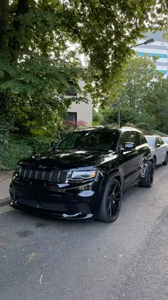 two black jeeps are parked on the side of the road in front of some trees