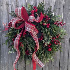 a christmas wreath hanging on a fence with red berries and greenery tied to it