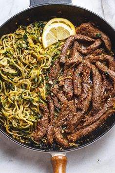 steak and noodles in a skillet with lemon wedges on the side for garnish