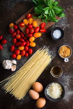 ingredients for pasta laid out on a table with tomatoes, basil, garlic and eggs