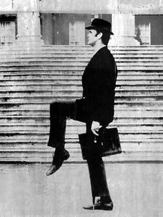 a black and white photo of a man walking in front of some steps with a briefcase