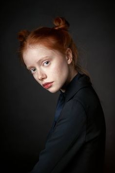 a woman with red hair is posing for the camera, wearing a black shirt and blue collar