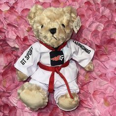 a stuffed teddy bear is dressed in karate attire and sitting on pink petals with a tag