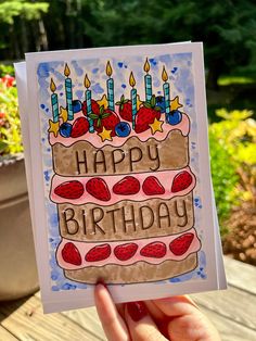 a hand holding up a birthday card that says happy birthday with candles and strawberries