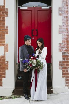 a man and woman standing in front of a red door