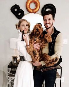 a man and woman holding a dog in front of a wall with donuts on it