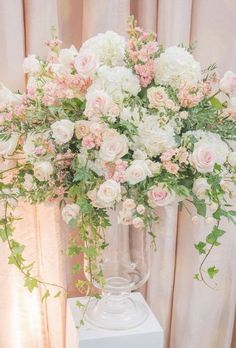 a vase filled with white and pink flowers on top of a table next to curtains