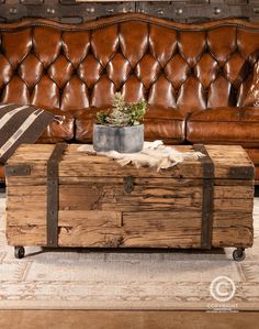 an old trunk sitting on top of a wooden table next to a brown leather couch