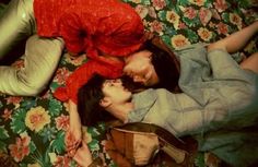 two people laying on a bed with flowers in the background and one person wearing a red shirt