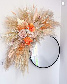 a mirror hanging on the wall next to a wreath with dried flowers and feathers in it