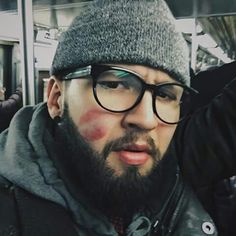 a man with red paint on his face wearing glasses and a gray beanie hat