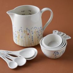 a pitcher, measuring spoons and cup on a brown tablecloth with flowers painted on it