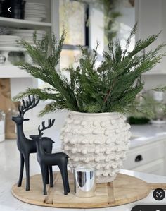 a white vase filled with green plants and two black deer figurines on top of a wooden tray