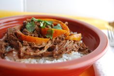 a red bowl filled with meat and rice on top of a yellow table cloth next to a fork