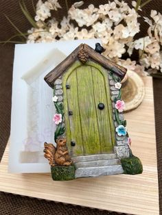 a small green door sitting on top of a wooden table next to flowers and a plate