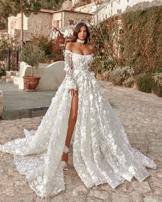 a woman wearing a white wedding dress with long sleeves and thigh high slits is posing for the camera